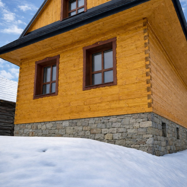 Detail drevenej stavby s obkladom s rybinovým spojom, kde presné stolárske spracovanie vytvára pevné a estetické spojenie masívneho dreva